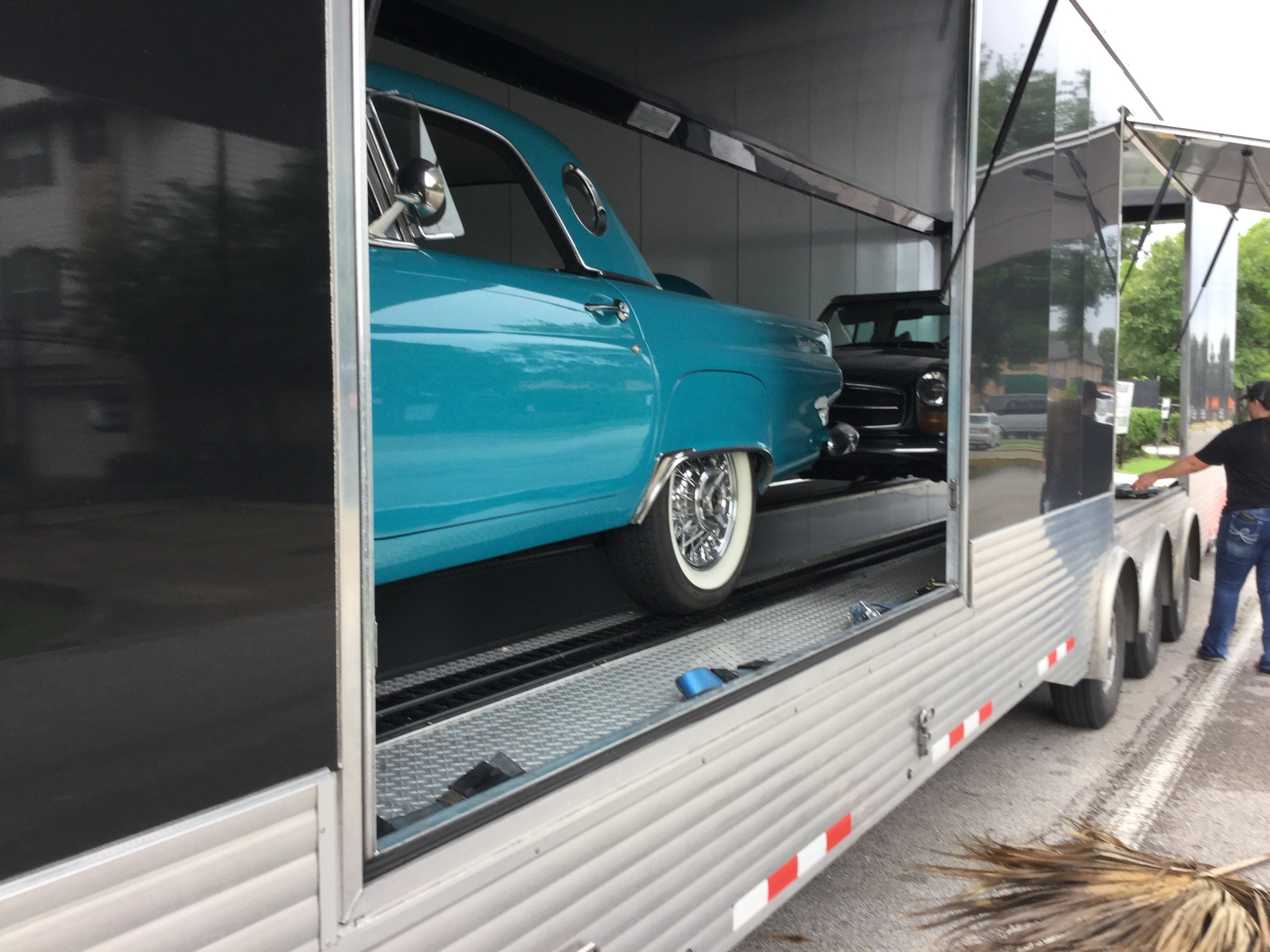 Trailer with a classic turquoise car inside, parked on a street.