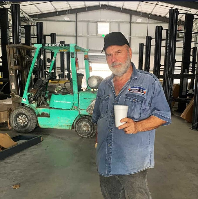 Man holding a cup in a warehouse with forklifts and car lifts in the background