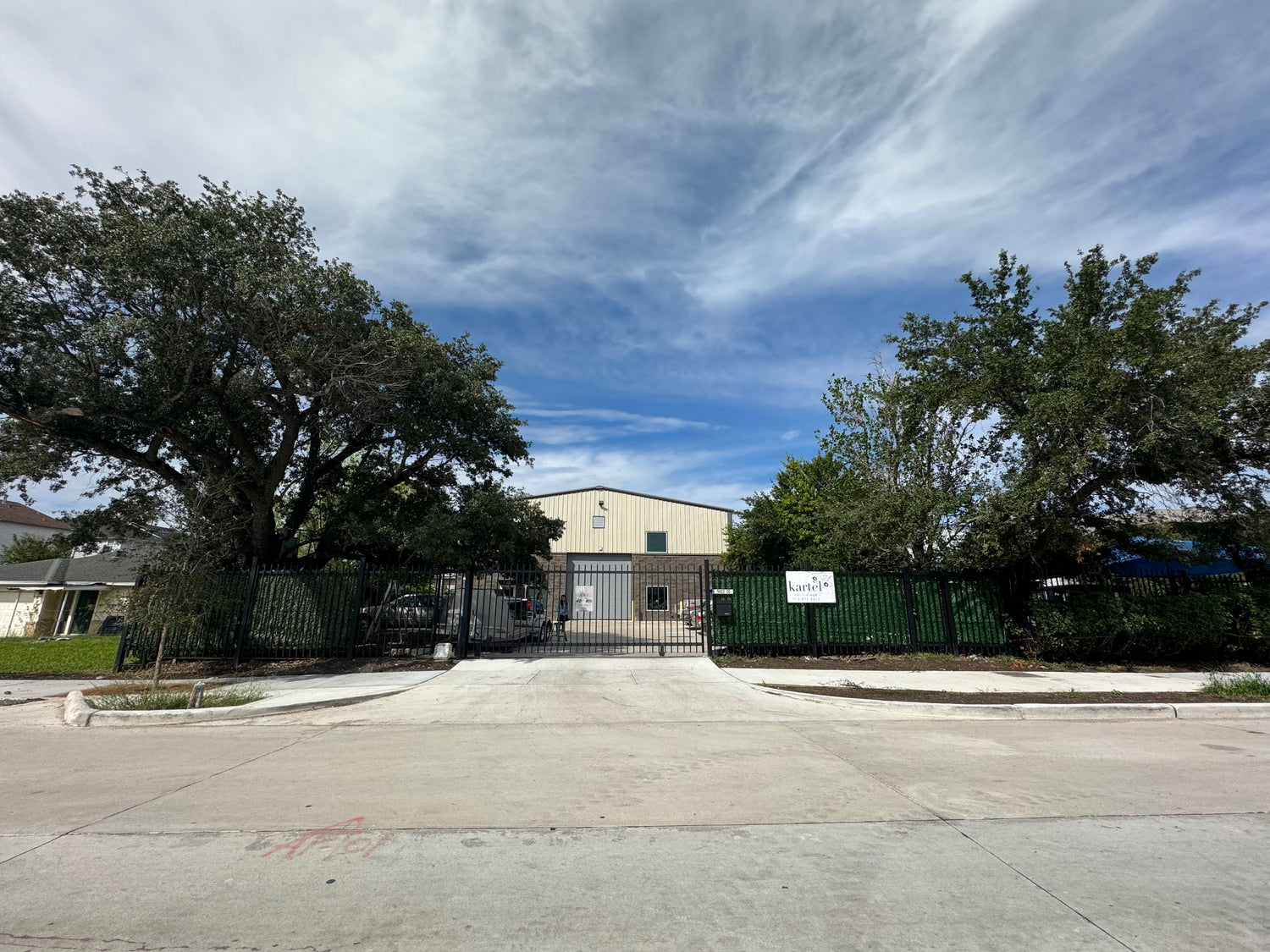 Commercial warehouse building with trees, black fence, and a clear sky