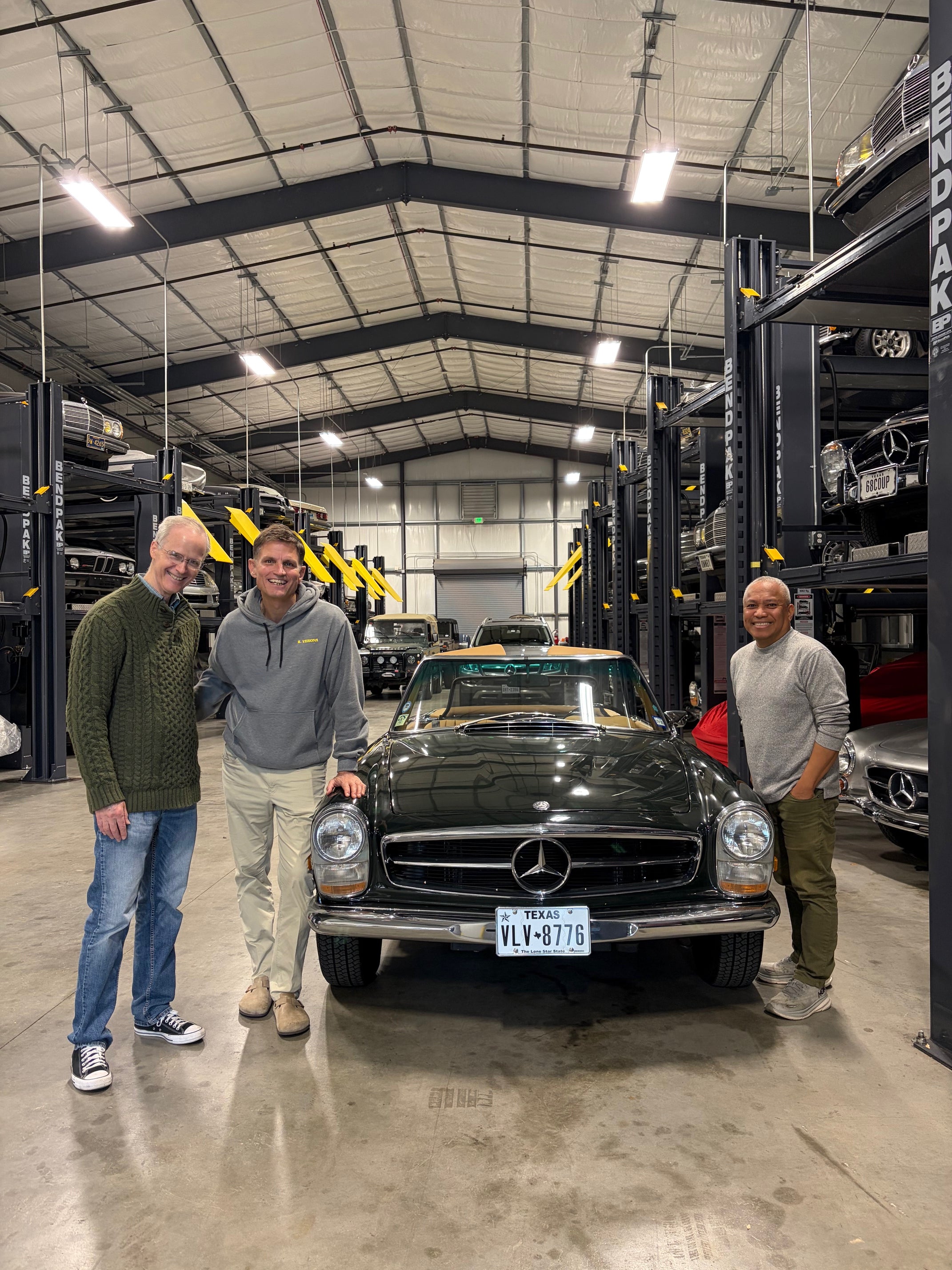 Three people standing next to a classic Mercedes-Benz in a car storage facility