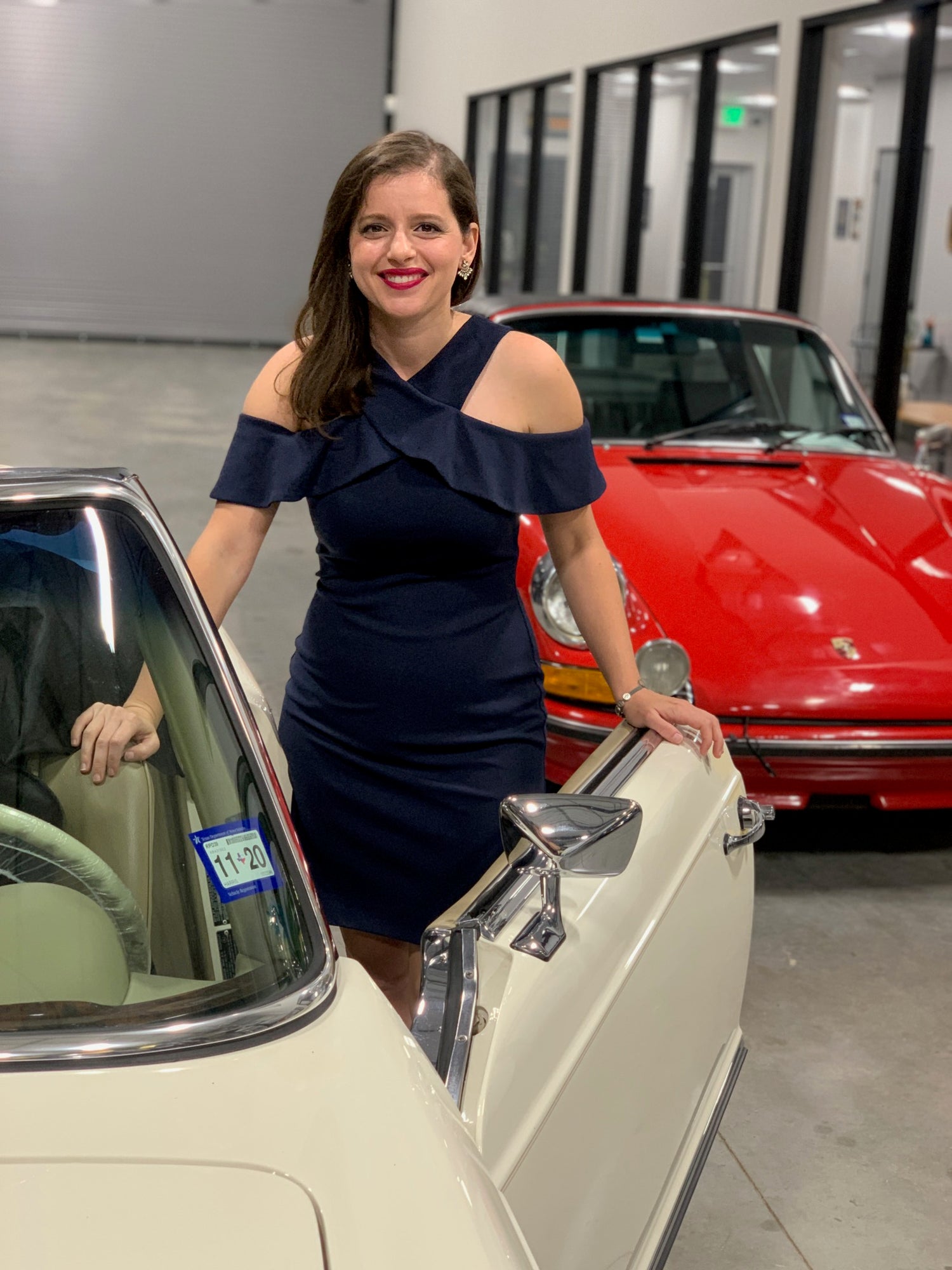 Woman in a navy dress standing next to a vintage car in a showroom.