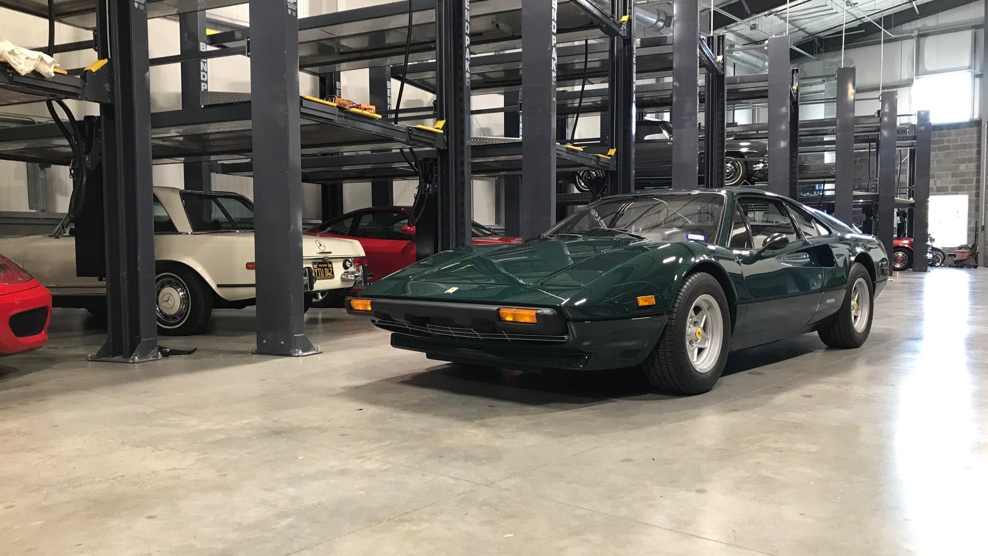 Green Ferrari inside a car storage facility with car lifts in the background