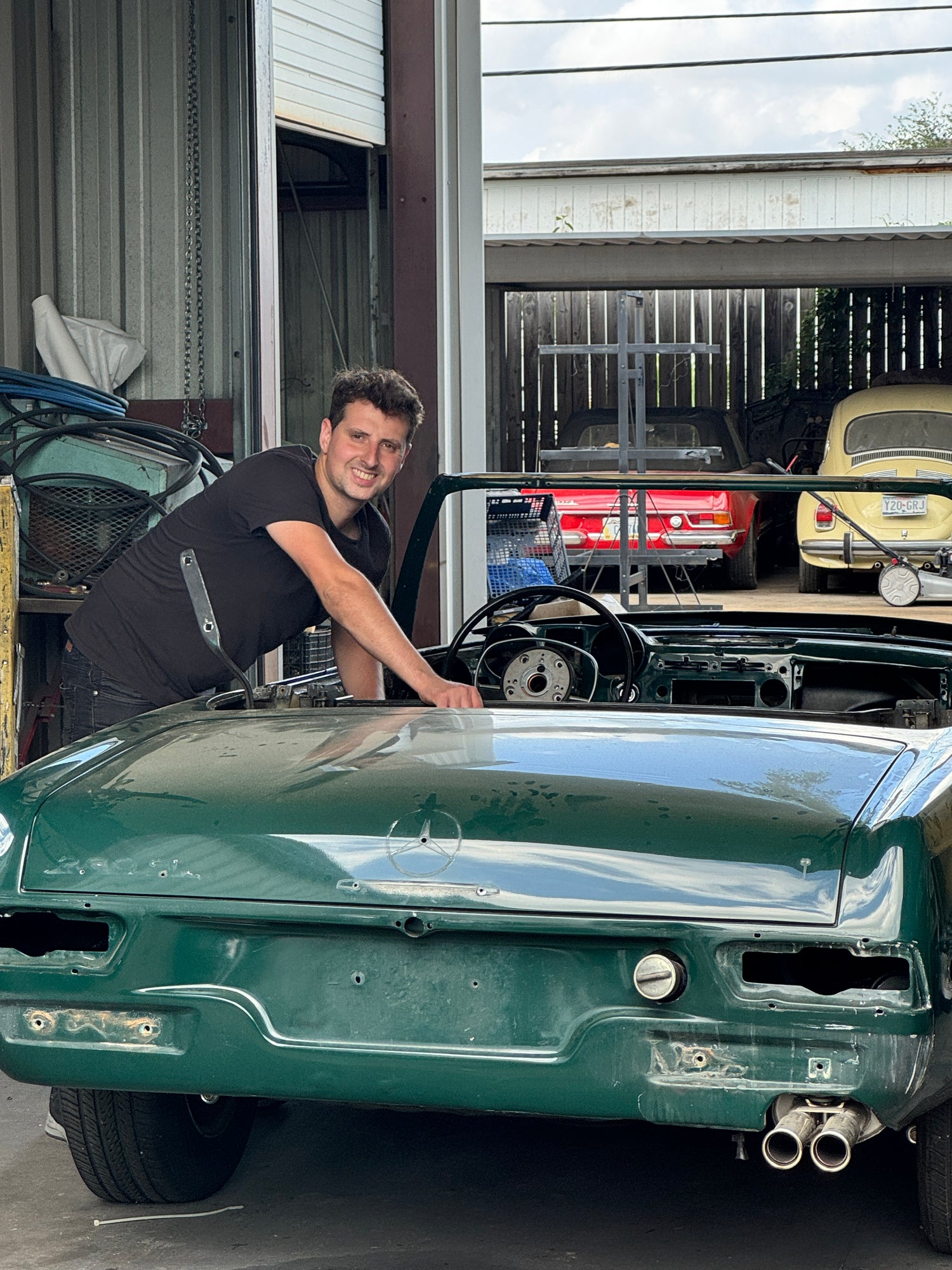 Mechanic leaning over the body of a classic green Mercedes convertible being restored