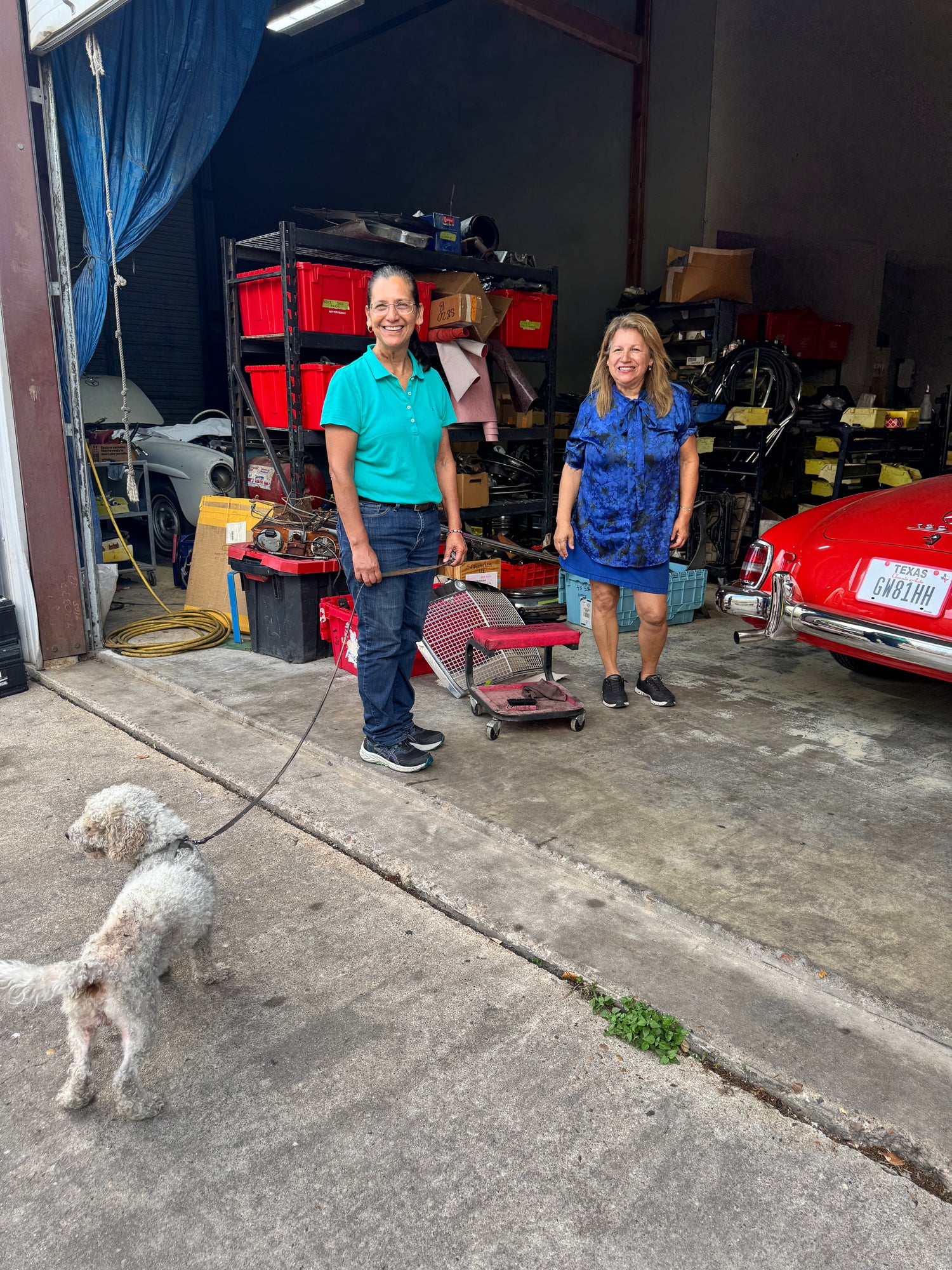 Two people and a dog standing next to a classic car filled with boxes and equipment at Kartel Car Storage & Social