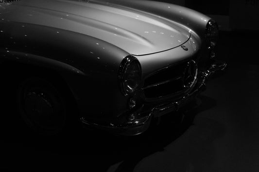 Close-up of a classic car's headlight and front grille in black and white.
